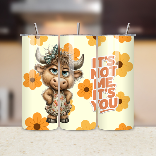 Tumbler with cartoon cow design and text 'It's not me, it's you' on a blurred background