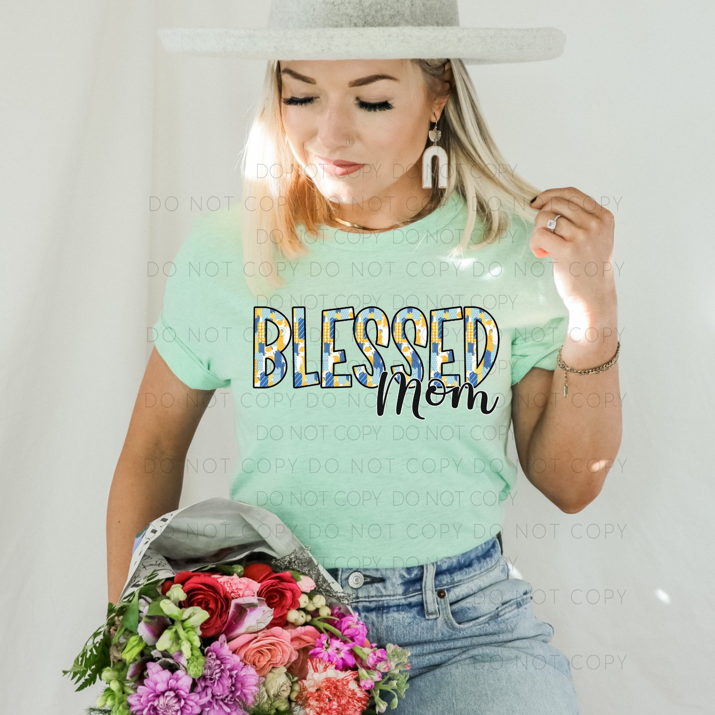 A woman wearing a light green unisex t-shirt with the text 'Blessed Mom' on it, holding a bouquet of flowers.