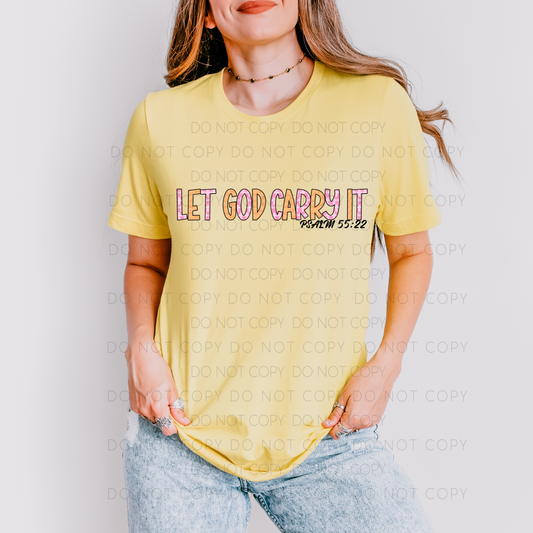 A person wearing a yellow unisex t-shirt with the text 'LET GOD CARRY IT' printed on the front.