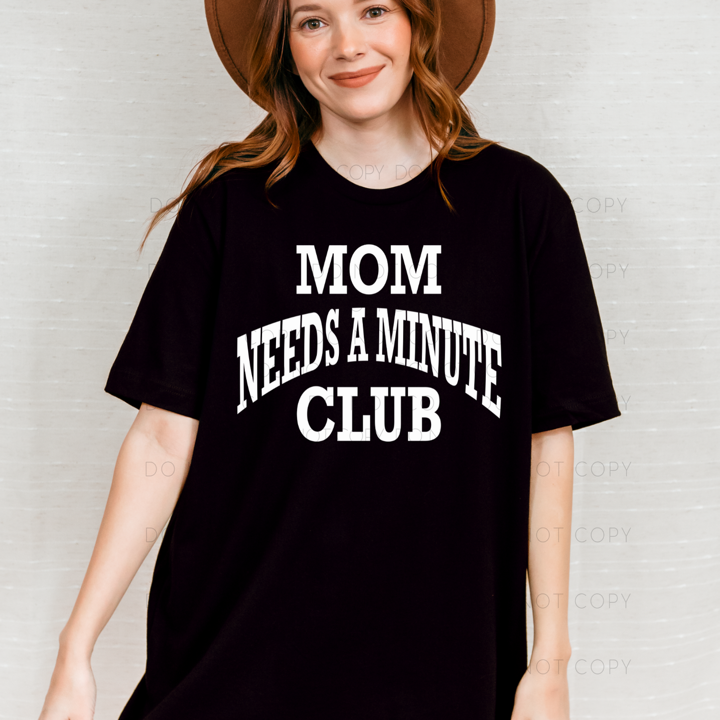 A woman wearing a black t-shirt with the text 'MOM NEEDS A MINUTE CLUB' in white letters.