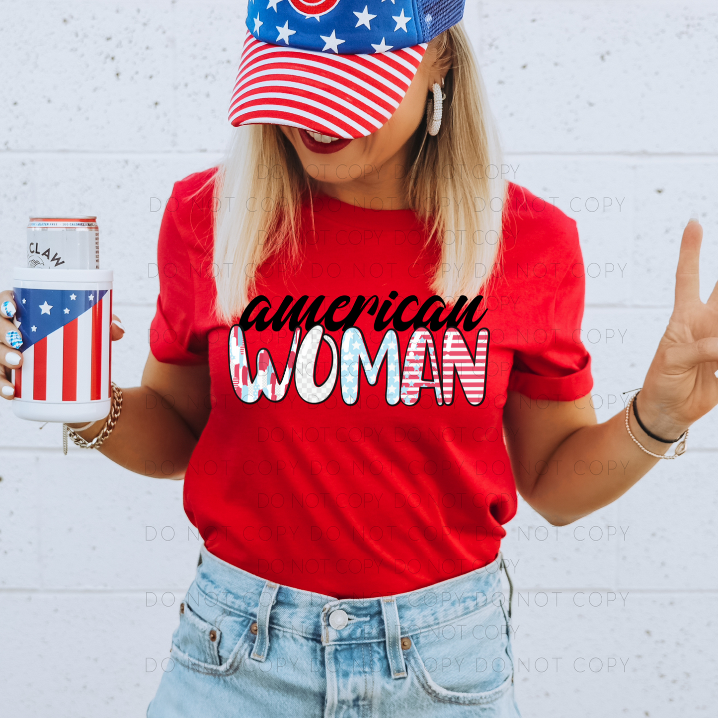 A person wearing a red t-shirt with the text 'american woman' on it, paired with a blue and white checkered hat and blue jeans. The person is holding a beverage can and making a peace sign.