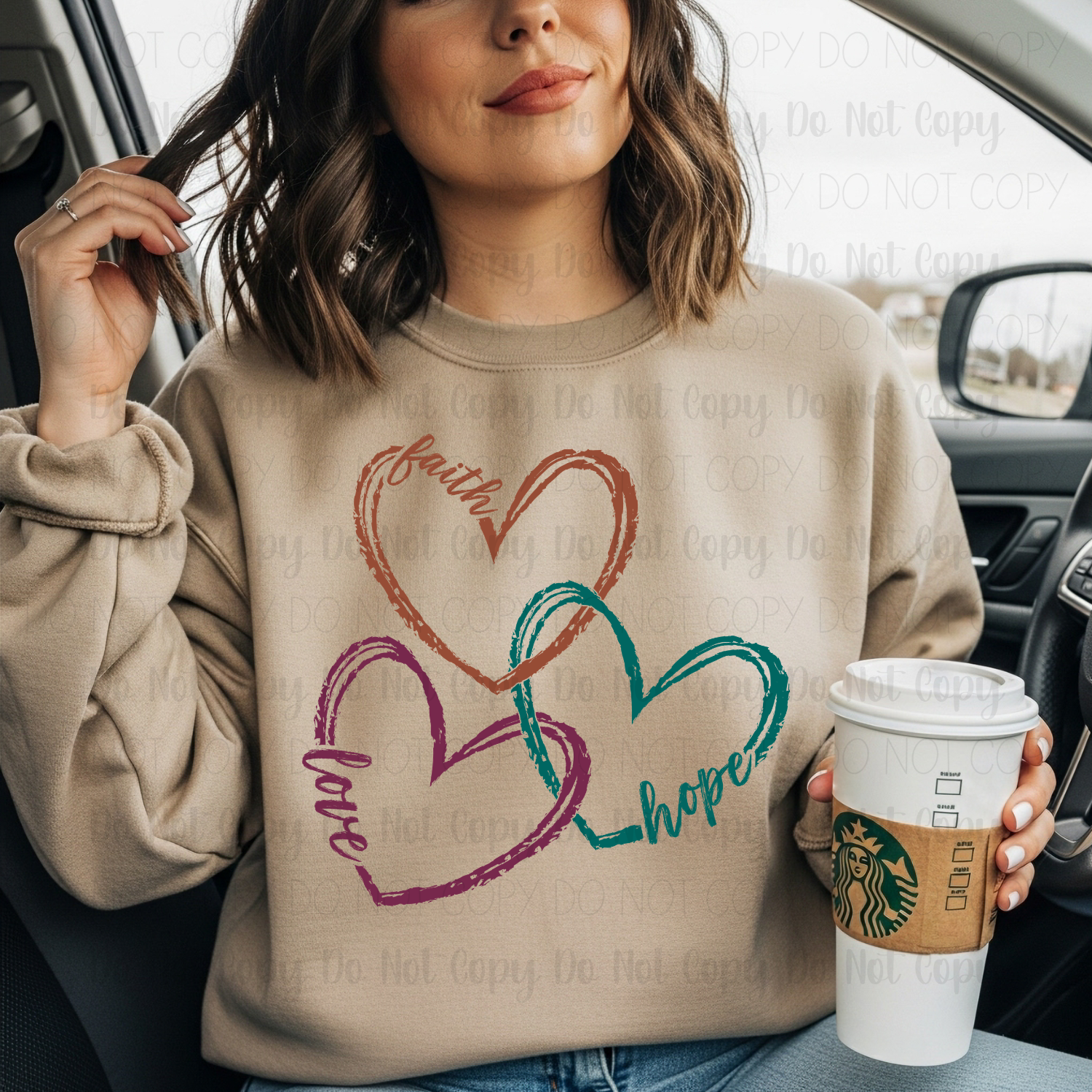 Woman wearing a beige sweatshirt with heart designs and text, holding a Starbucks cup.