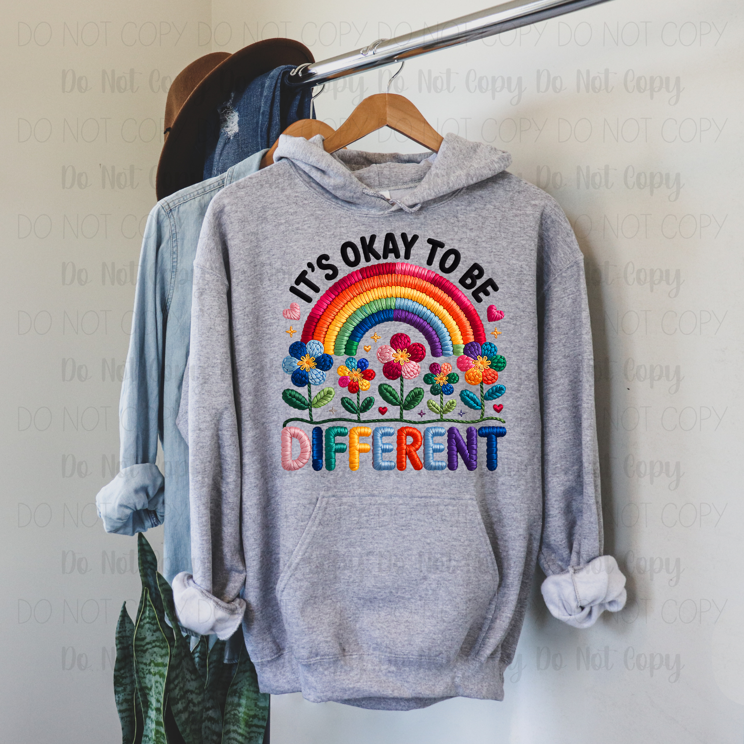 Gray hoodie with colorful text and rainbow design on a hanger against a white wall.