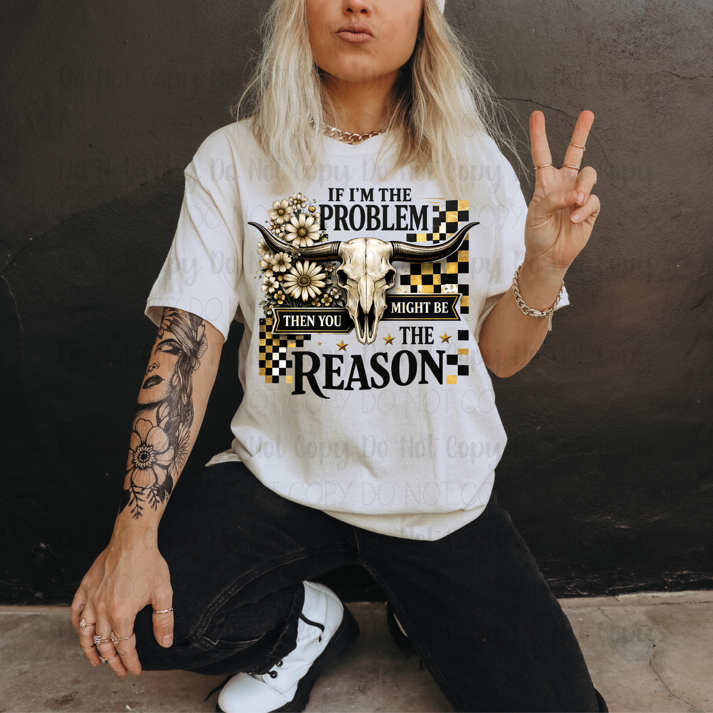 Person wearing a white t-shirt with a graphic design and text, sitting against a dark wall.
