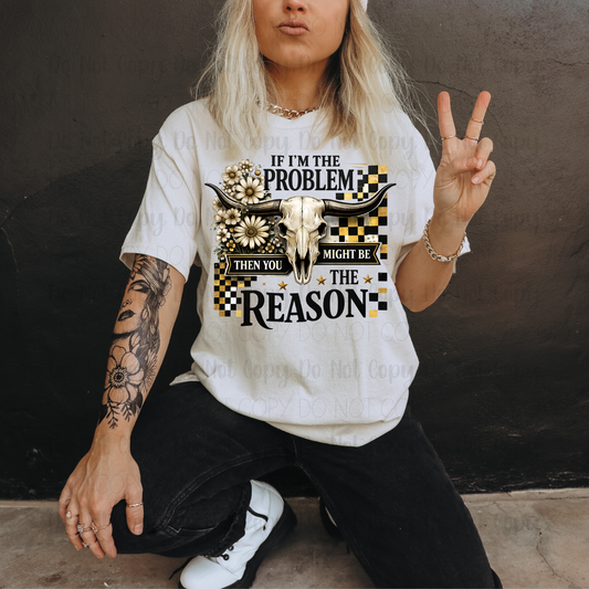 Person wearing a white t-shirt with a graphic design and text, sitting against a dark wall.